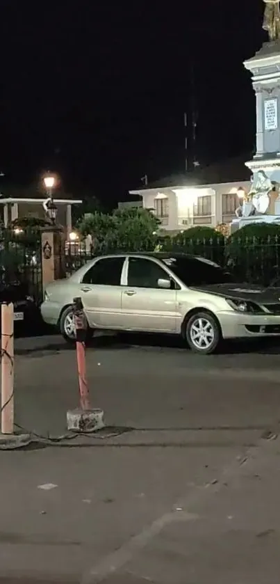 City street at night with a car parked near a monument.