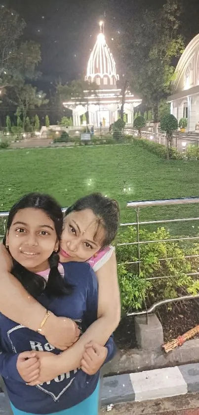 Mother and daughter embrace in park with temple in background.