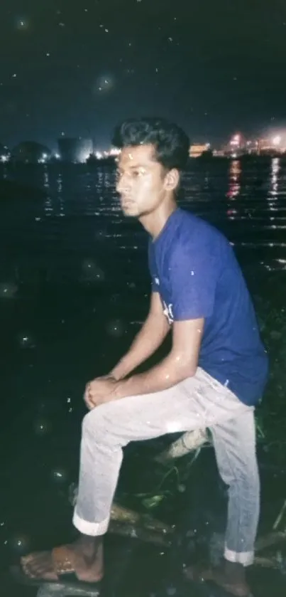 Young man in blue shirt by moonlit river at night.