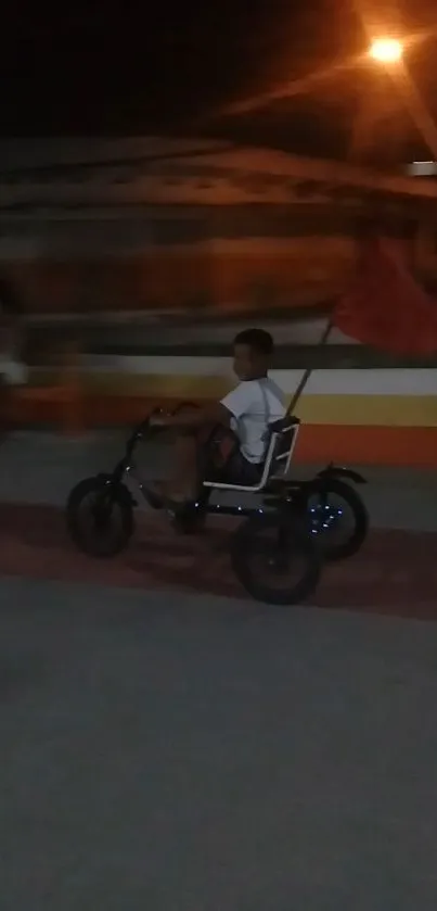 Boy riding tricycle at night under streetlight.