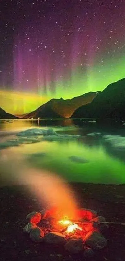 Vibrant aurora borealis over a campfire by a mountain lake at night.