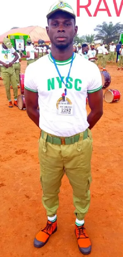 NYSC member standing proudly in full uniform on parade ground.