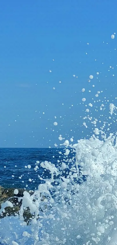 Ocean wave splashing on rocks under clear blue sky in mobile wallpaper.