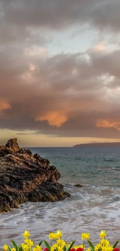 Sunset over ocean with rocks and flowers on the shore.