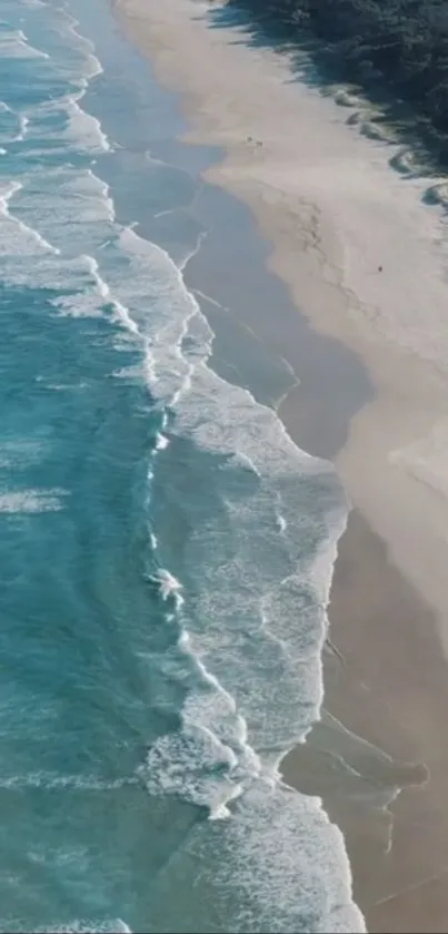 Aerial view of ocean waves crashing on a sandy beach with blue and white tones.