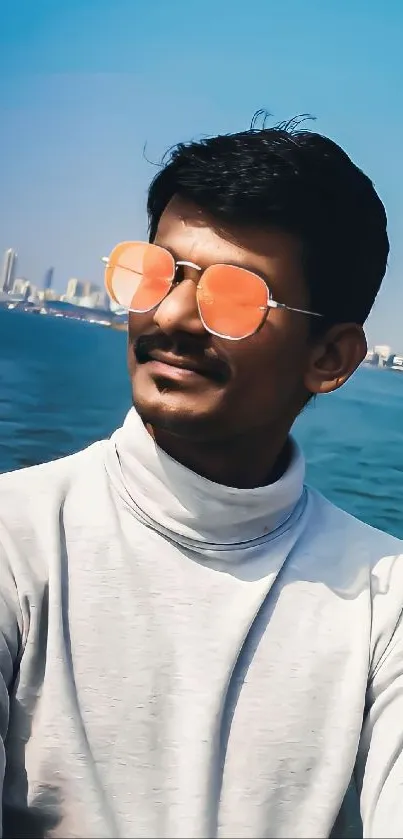 Man in sunglasses with ocean and city backdrop.