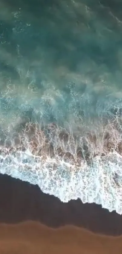 Aerial view of calming ocean waves hitting the shoreline in beautiful shades of blue.