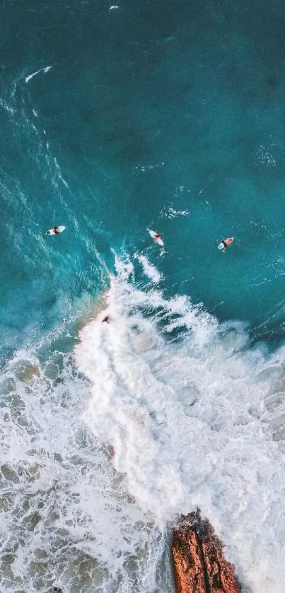 Aerial view of turquoise ocean waves crashing on a rocky shore with surfers nearby.