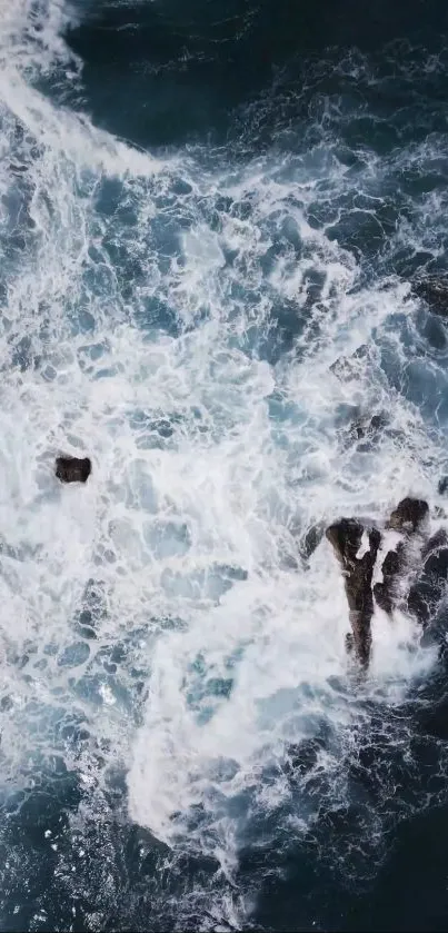 Aerial view of ocean waves crashing against rocks with swirling sea foam.