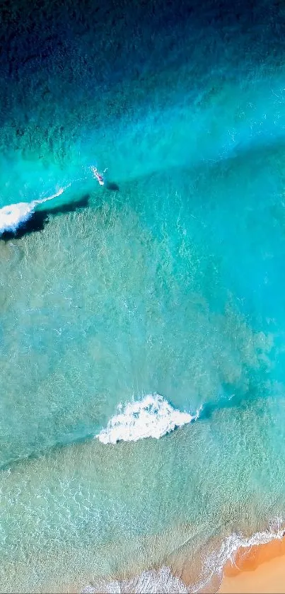 Aerial view of ocean waves hitting a sandy beach with vibrant turquoise hues.