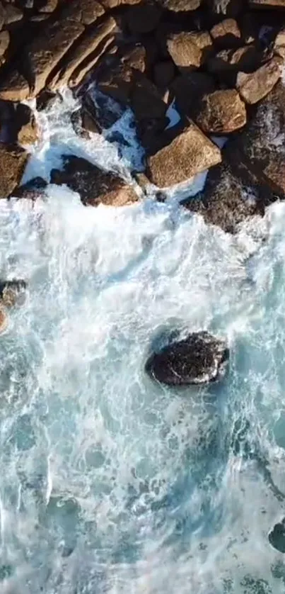 Aerial view of ocean waves crashing onto a rocky shoreline with vibrant blue water.