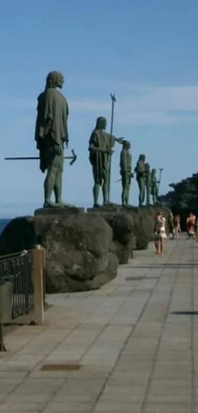 Statues by the ocean on a stone walkway with a clear blue sky.