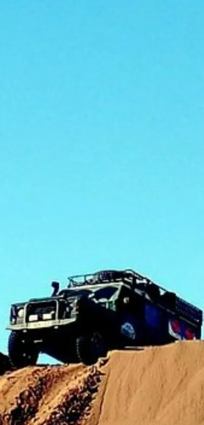 Off-road truck on desert dune under blue sky.