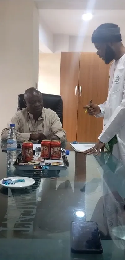 Office meeting with beverages on table and two men in discussion.