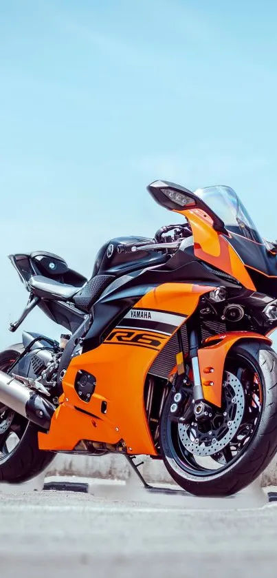 Orange and black sports bike on open road under blue sky.