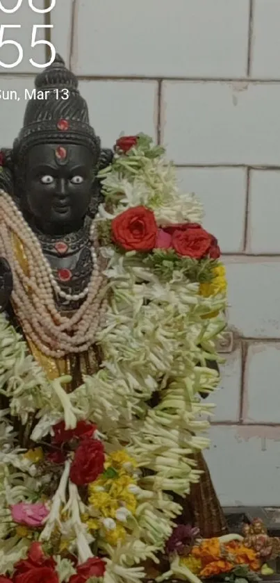 Ornate deity statue with floral garlands on tiled background.