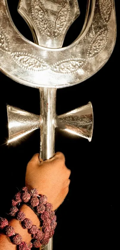 Silver trident held by hand with rosary on black background.