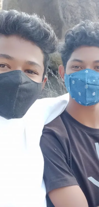 Two friends in masks outdoors with rocky background.