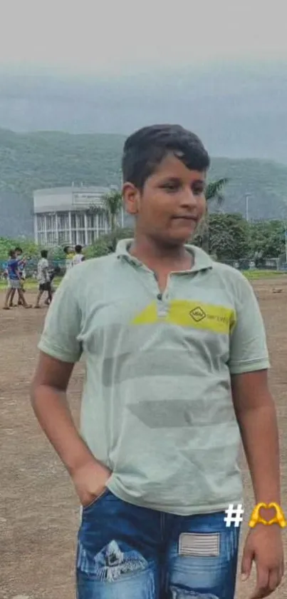 Boy standing in a natural outdoor setting with mountains and greenery.