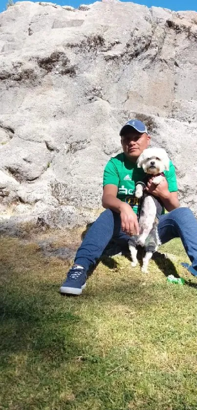 Man with dog sitting under a rocky cliff.