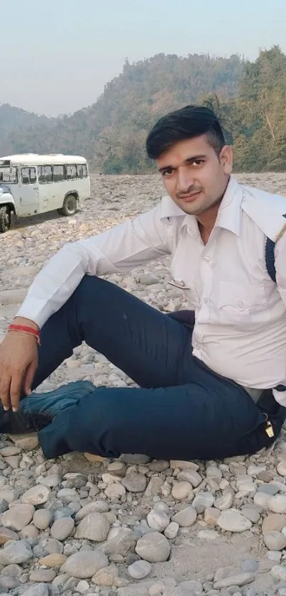 Man sitting on rocky terrain with a jeep in the background.