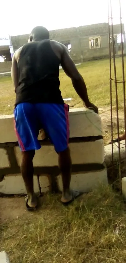 Man in athletic wear working at outdoor construction site with brick wall.