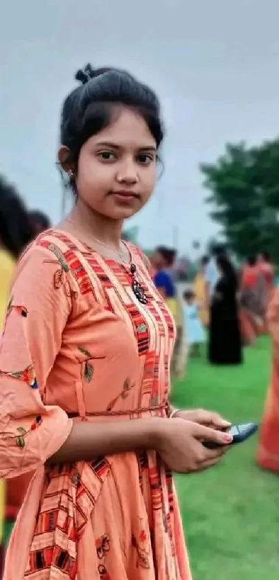 Young woman in peach dress at outdoor event, vibrant background.