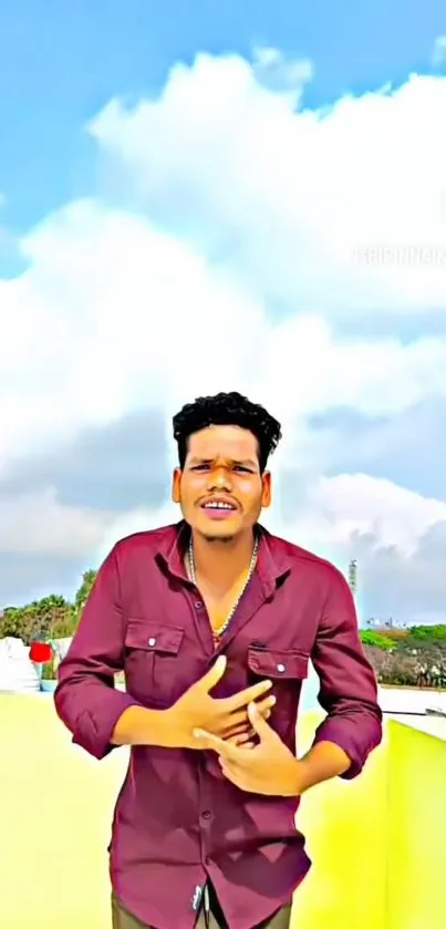 Man in maroon shirt stands outdoors against a bright, cloudy sky.