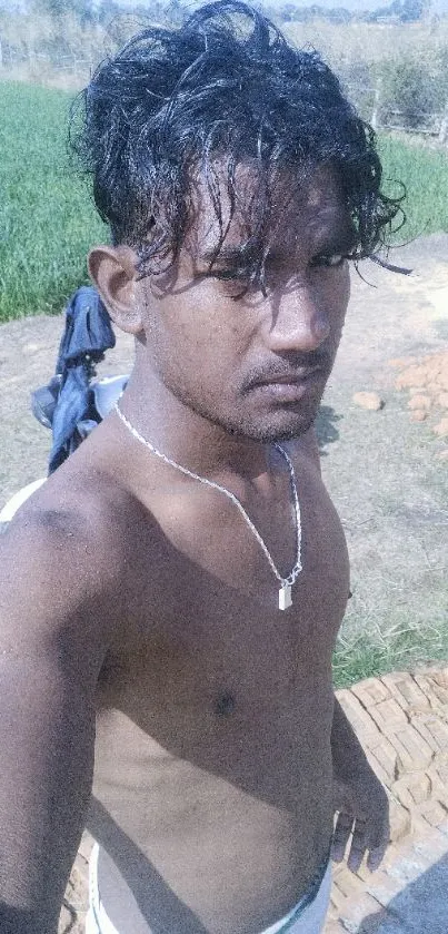 Outdoor rural selfie with greenery and clear sky backdrop.