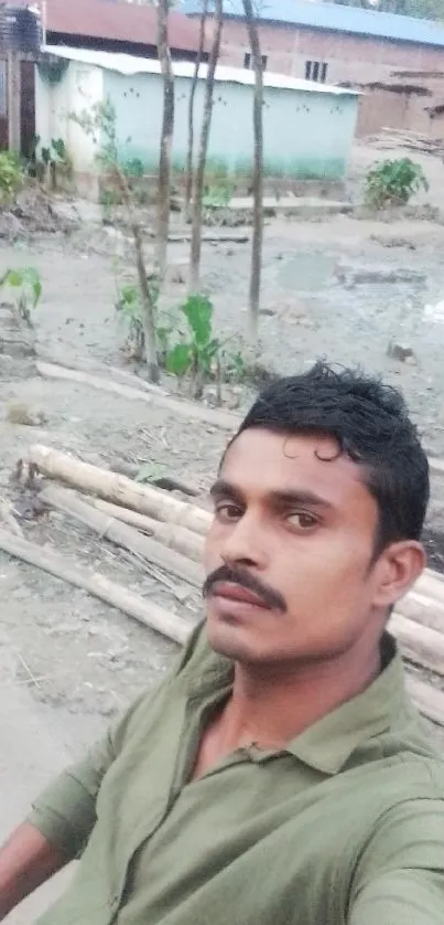 Selfie of a man in green shirt outdoors with rustic background.