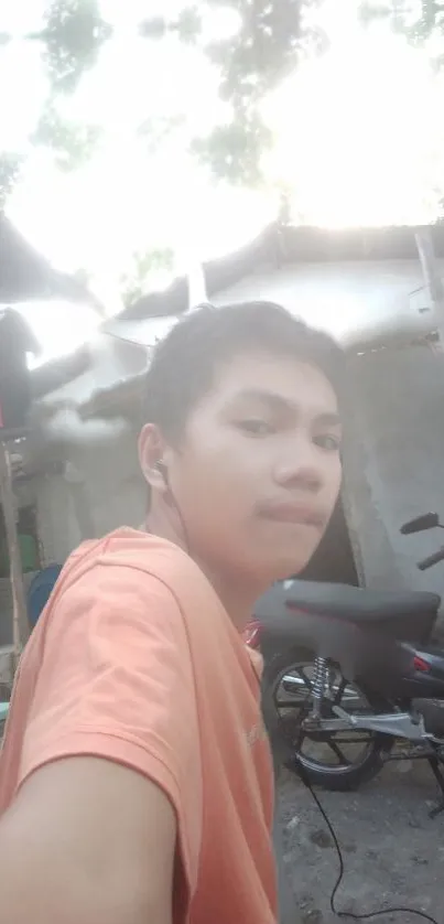 Outdoor selfie with orange shirt and motorcycle in background.