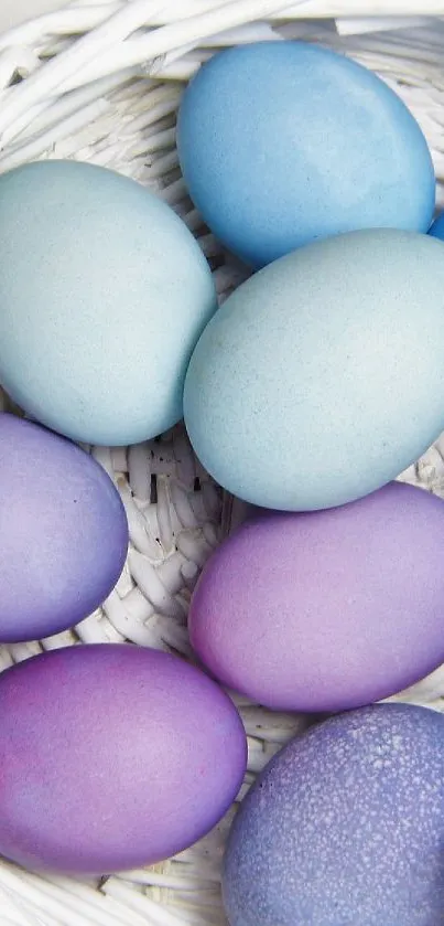 Pastel colored eggs in a white basket with purple flowers on a bright background.