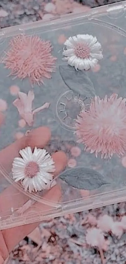 Hand holding a CD case with pastel pink and white flowers inside on a blurred background.