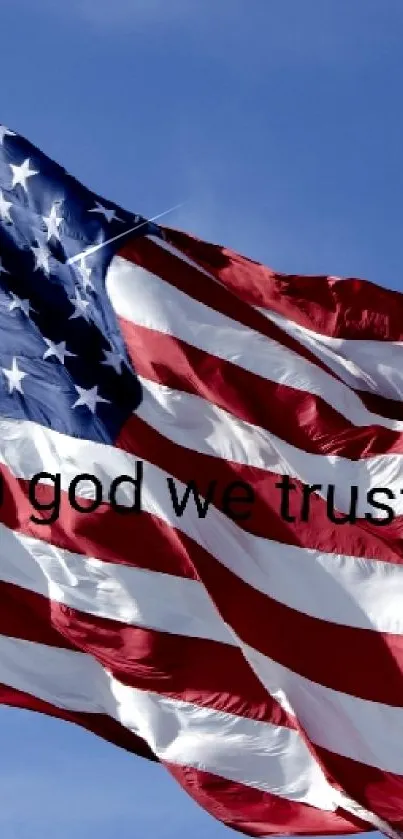 Waving American flag with 'In God We Trust' text on blue sky.