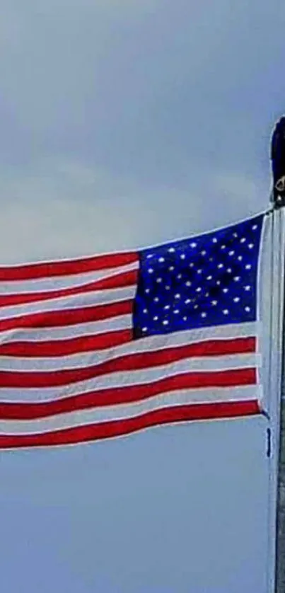 American flag with eagle perched on flagpole under blue sky.