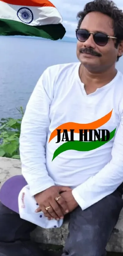 Man with 'Jai Hind' shirt posing by Indian flag.