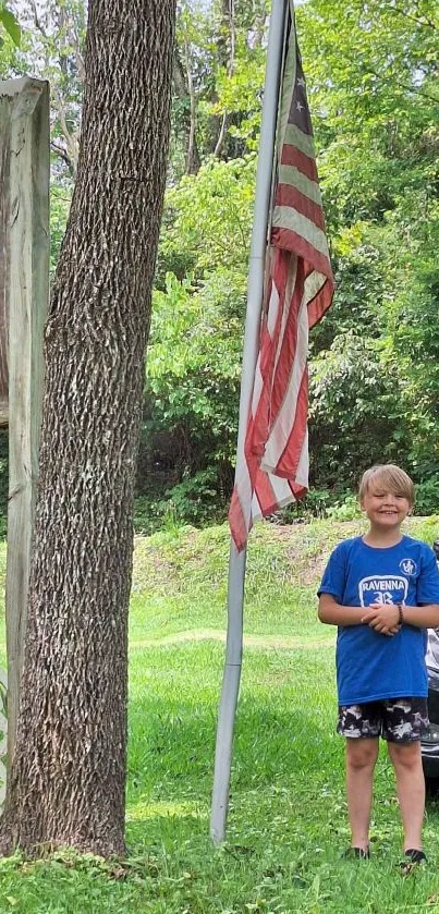 Child stands next to American flag in lush outdoor setting.