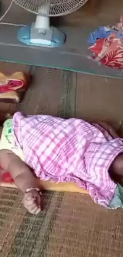 Baby sleeping on mat with pink blanket.