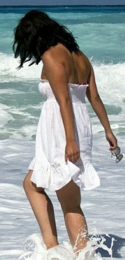 Woman in white dress walks along the turquoise beach waves.