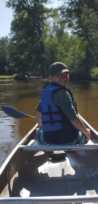 Person canoeing on a peaceful river surrounded by trees.