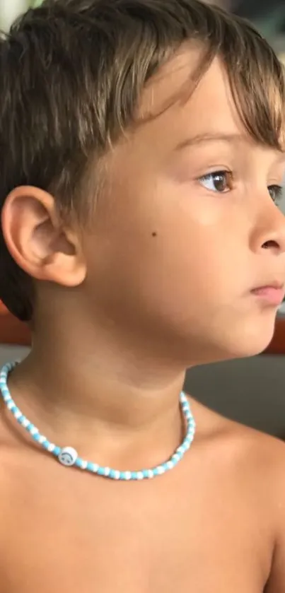 Child with blue necklace in a thoughtful pose, in natural lighting.