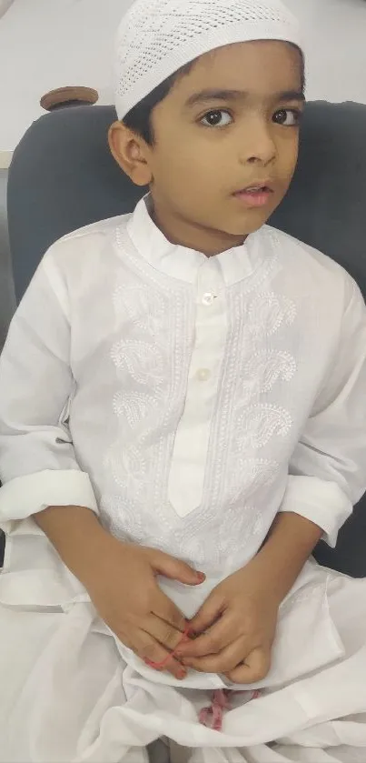 Young child in traditional white attire seated calmly.