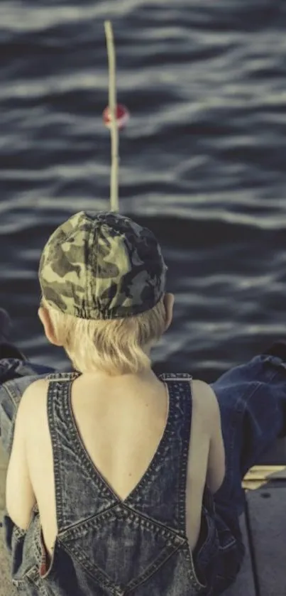 Child with camouflage hat sitting on a dock, fishing by the water.