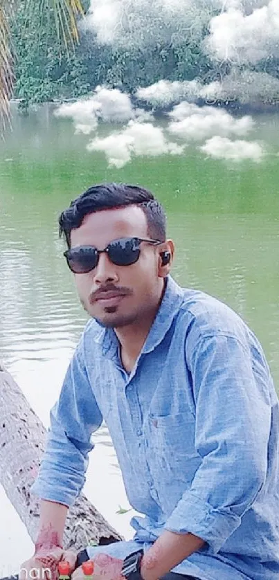 Man sits by a serene lake under a palm tree, enjoying a peaceful view.