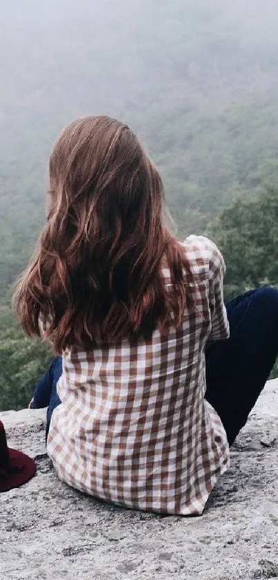 Woman sitting on a rock with a tranquil green landscape.