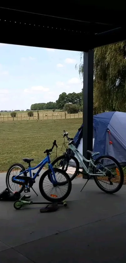 Tranquil camping scene with bikes and tent in a green field under a blue sky.