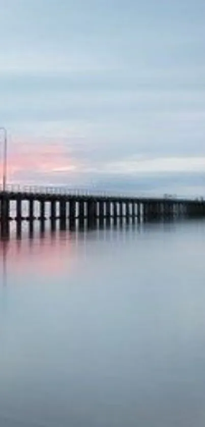 A serene pier stretching into calm waters at sunset with a clear sky.