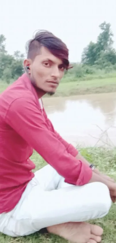 Man sitting by a reflective riverbank in nature.