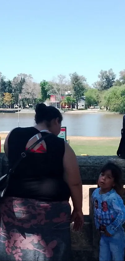 Woman and child by a calm riverside under a clear blue sky.