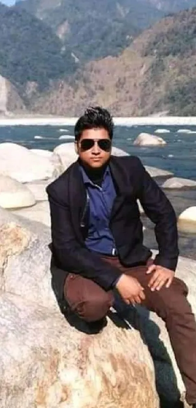 Person sitting on riverbank surrounded by rocks and mountains.